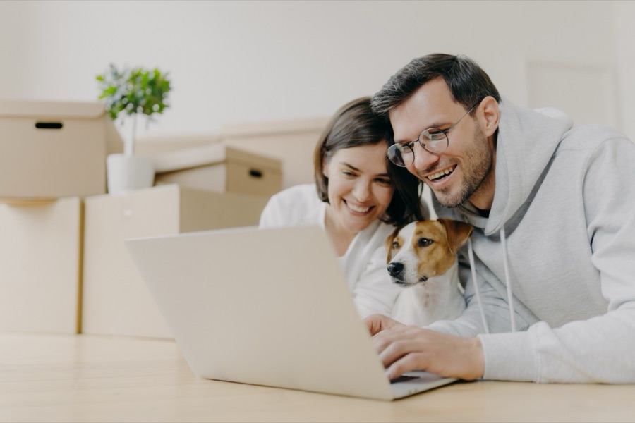 A couple and their terrier at a laptop, moving boxes behind them
